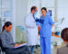 Dentist showing teeth x-ray reviewing it with nusre. Doctor and assistant working in modern crowded stomatological clinic, patients sitting on chairs in reception filling in dental forms and waiting